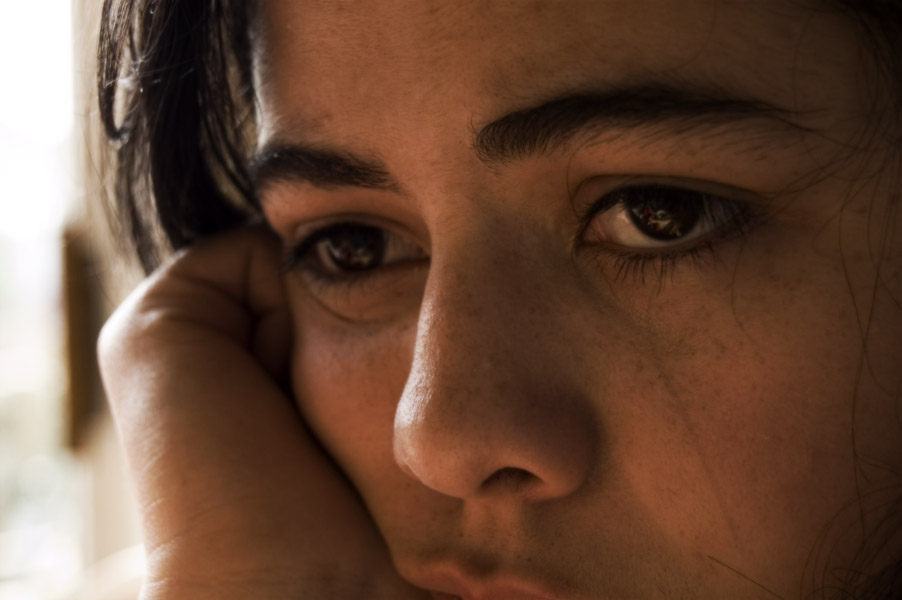 A zoomed in image of a grief-stricken white woman staring off in the distance with tears in her eyes.